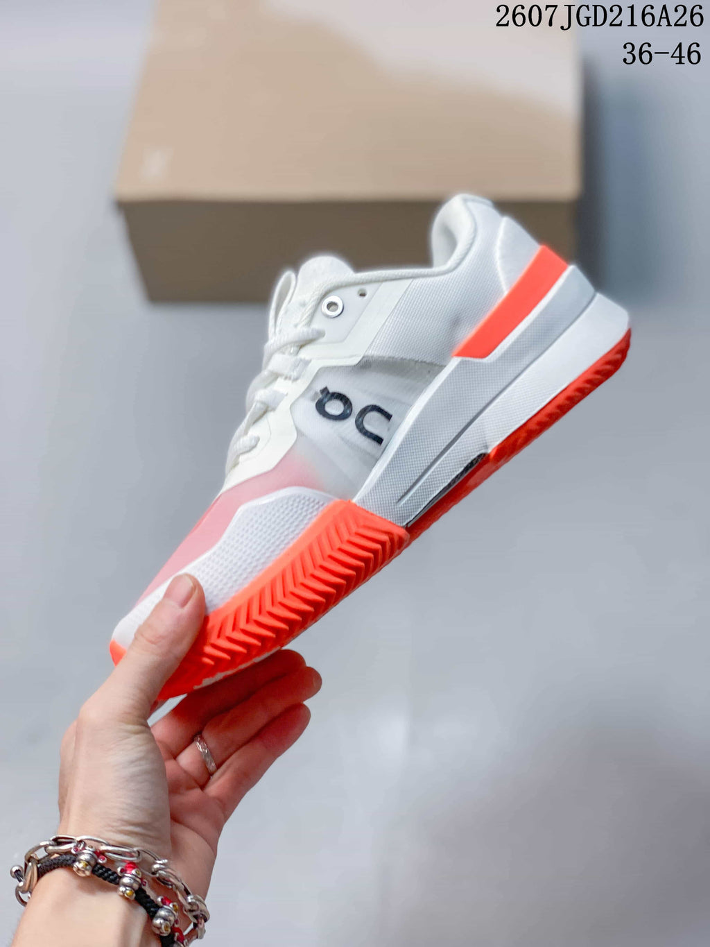 Side view of the white low-top sneaker with On branding, pink forefoot panel, orange heel accent and orange outsole.