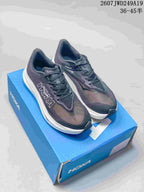 Pair of dark Hoka running shoes displayed on a blue shoe box, showing the mesh upper, white midsole and visible style code text.