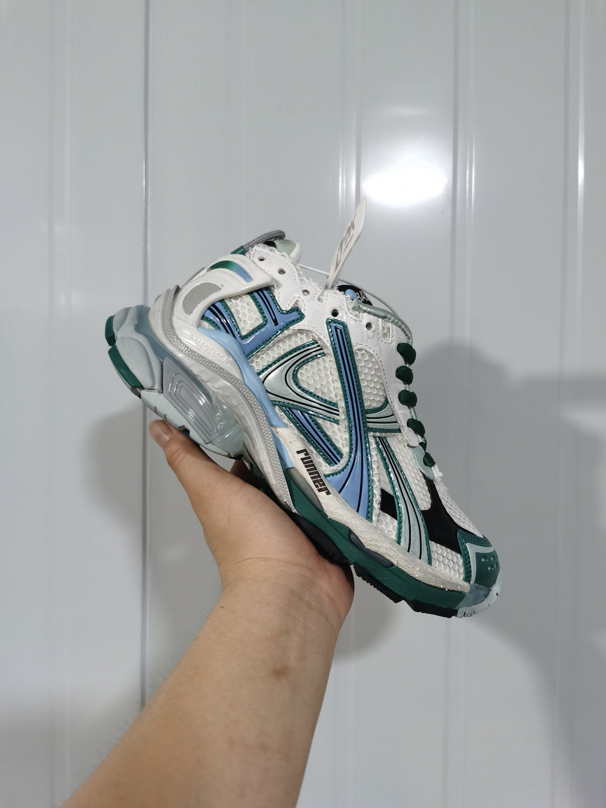 Balenciaga Runner sneaker held in hand, showing the white, emerald green, blue, and black layered upper.