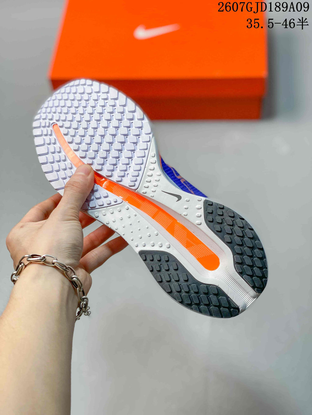 Underside view of the shoe showing a white and black segmented rubber outsole with an orange central accent.