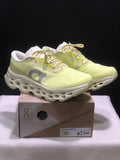 Pair of light yellow and white On Cloudmonster 3 sneakers displayed on their box.