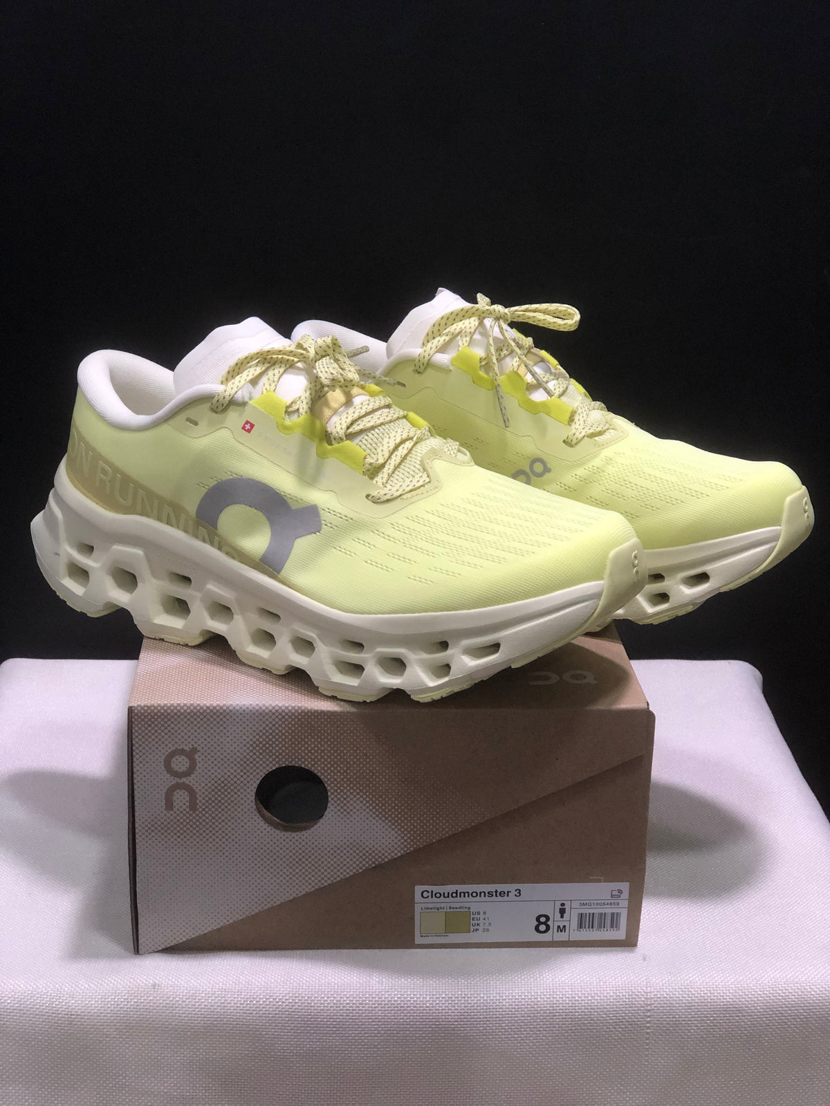 Pair of light yellow and white On Cloudmonster 3 sneakers displayed on their box.