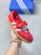 Angled view of the red and white Samba Jane sneaker showing the strap, white stripes, contrasting toe panel, and gum sole.