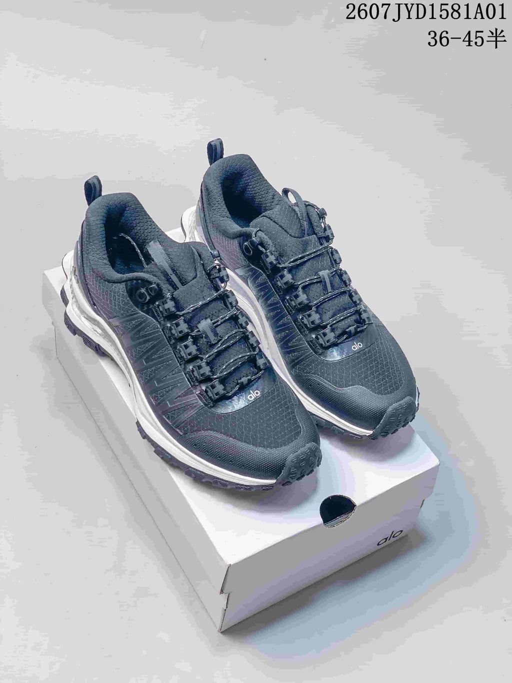 Black Alo Trail sneakers with textured uppers and treaded outsoles on a shoebox.