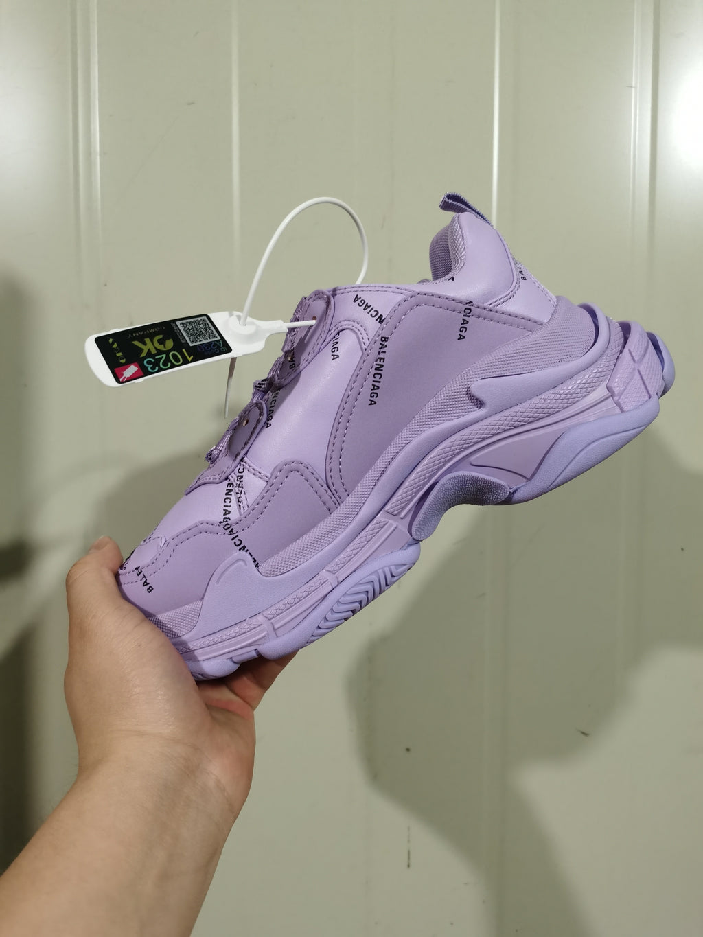 Rear three-quarter view of the purple Balenciaga Triple S sneaker with a hanging tag.