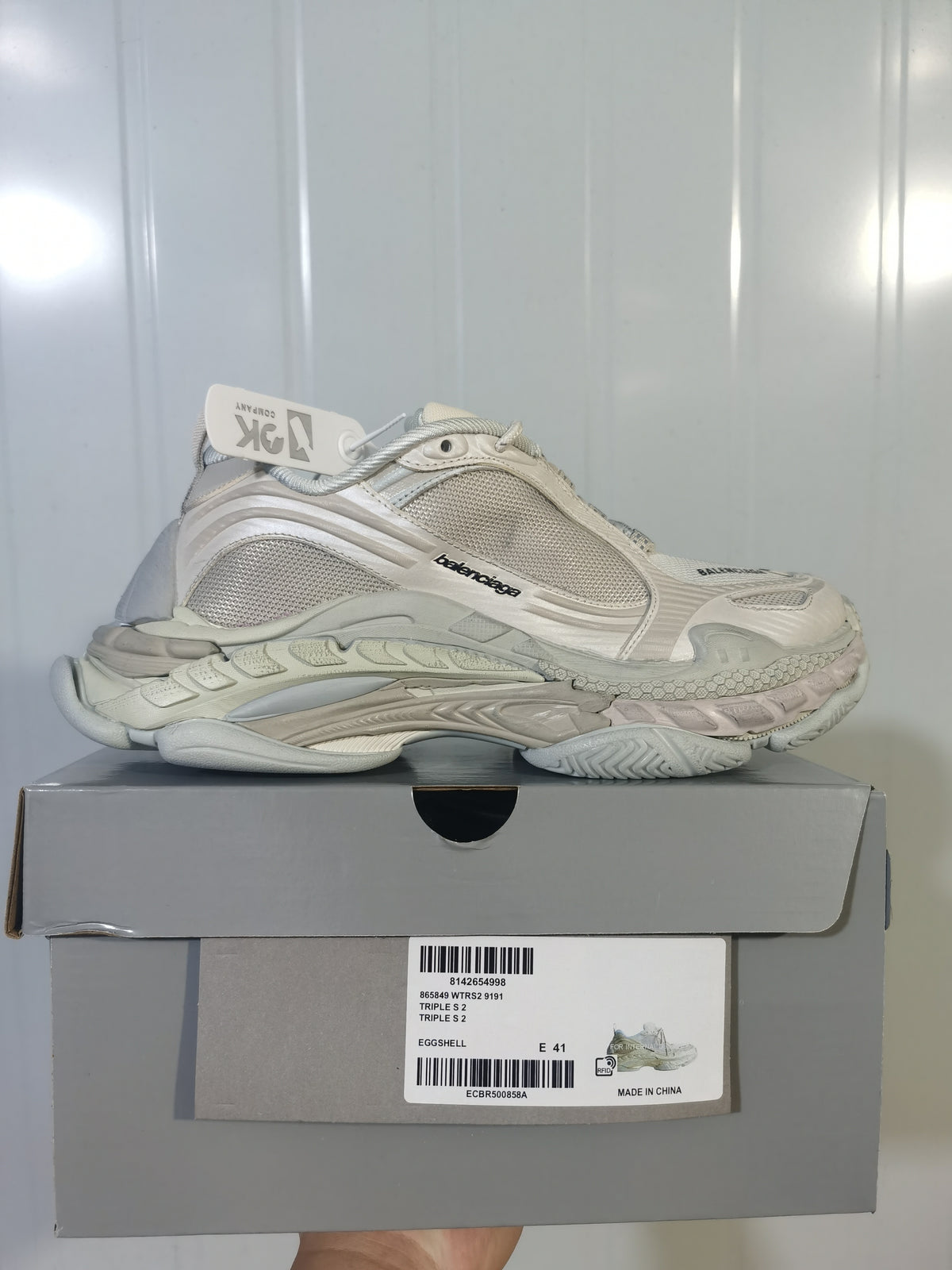 Side view of an off-white Balenciaga sneaker resting on its box; the label shows "TRIPLE S 2" and size "E 41".