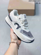 Angled side view of the white, gray, and navy On sneaker showing its layered upper and dark outsole.