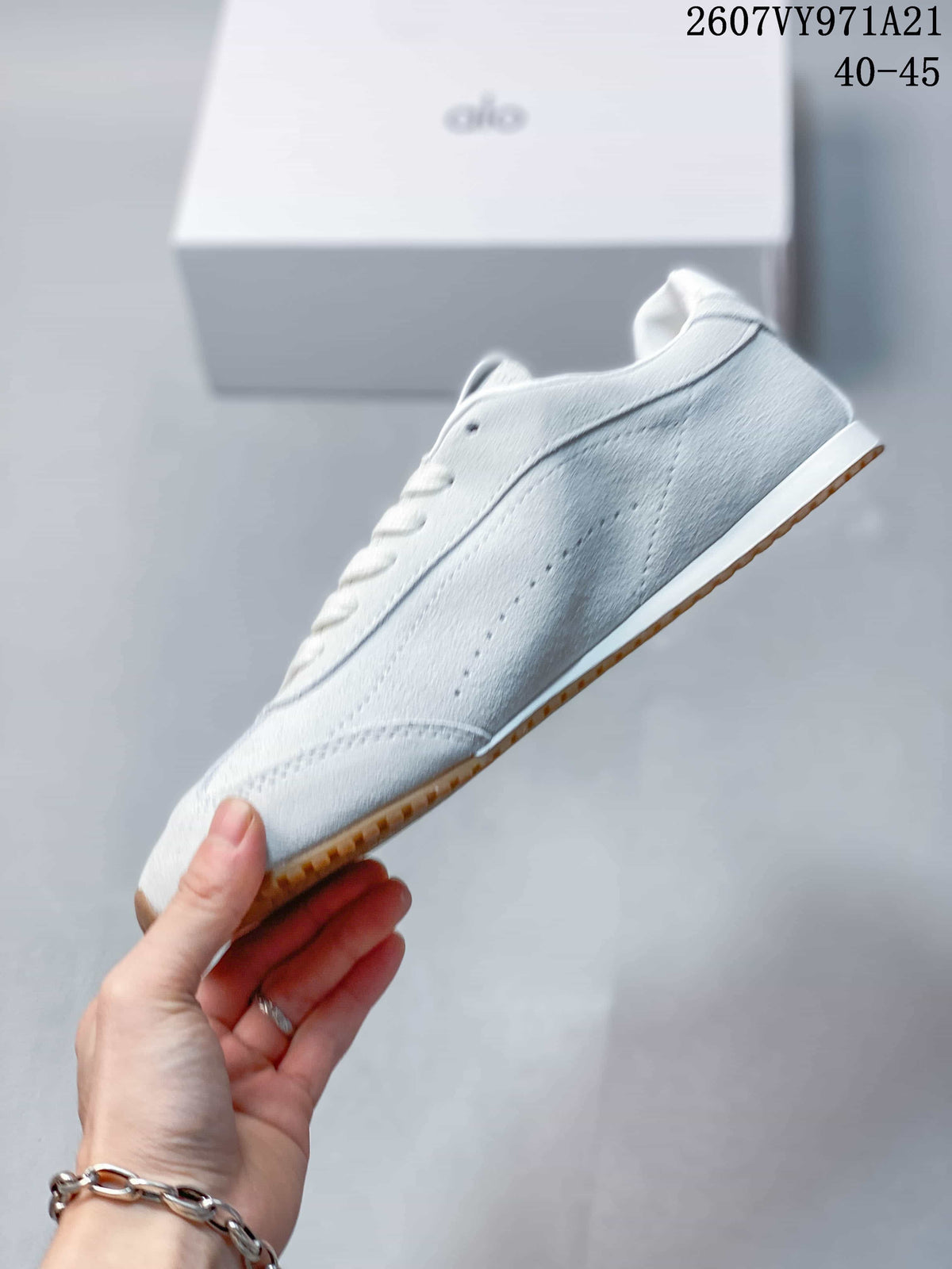 Side profile of the white low-top sneaker showing tonal stitched panels, small perforations, and the gum-colored outsole.
