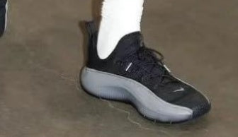 Black Nike low-top sneaker with a gray sole, shown worn with a white sock