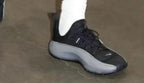 Black Nike low-top sneaker with a gray sole, shown worn with a white sock