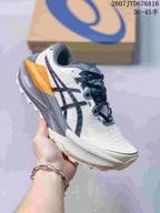 Angled side view of the ASICS Trabuco Max 5 with white upper, navy branding, gray midsole, and orange heel details.