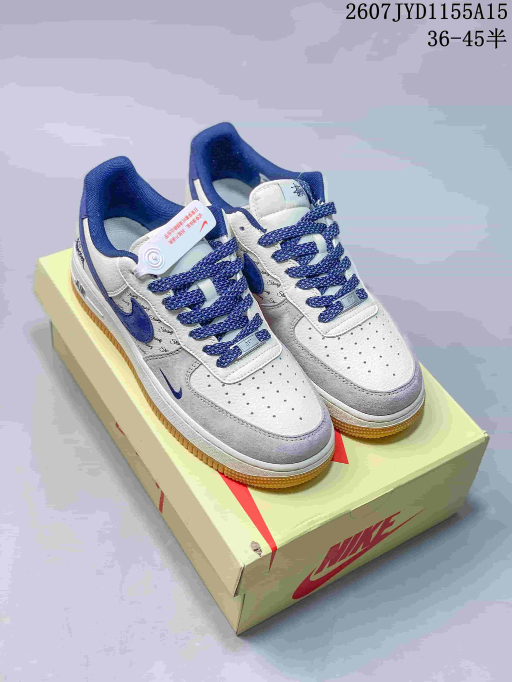 Pair of white, grey and blue Nike Air Force 1 sneakers displayed on a Nike shoe box, with the style code and size range visible at the top.