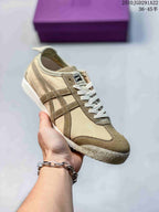 Beige and brown Onitsuka Tiger sneaker held in hand, showing contrast stripes and a textured outsole.