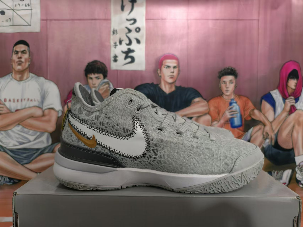 Side view of a silver Nike basketball shoe with a large stitched Swoosh and gold-tone accent