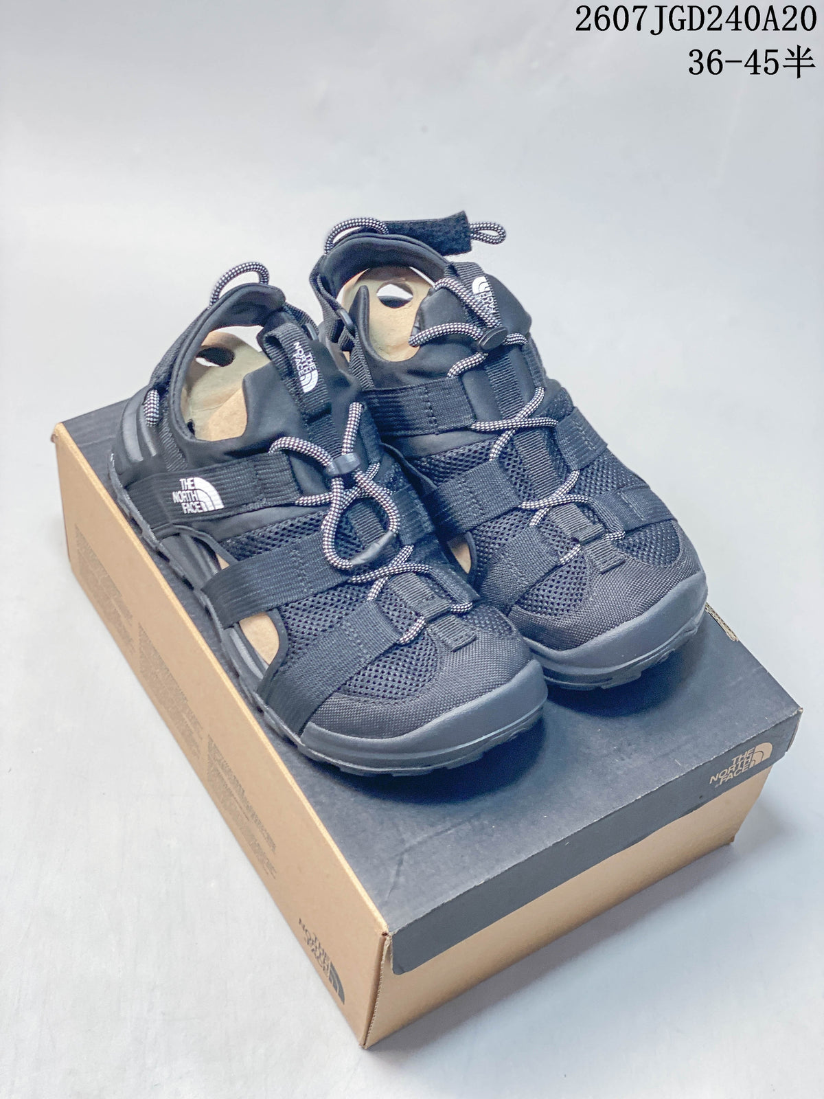 Pair of black The North Face Cedar Measa sandals displayed on a shoe box, showing the open-toe construction, adjustable straps, and cord-style lacing.