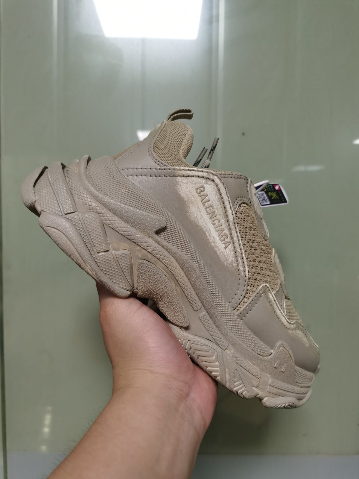 Side view of a light beige Balenciaga Triple S sneaker showing layered panels, mesh sections, branded side detailing, and a chunky textured sole.