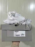 White Nike sneaker displayed on its box, showing the side profile, layered upper, chunky outsole, and box label.