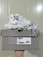 White Nike sneaker displayed on its box, showing the side profile, layered upper, chunky outsole, and box label.