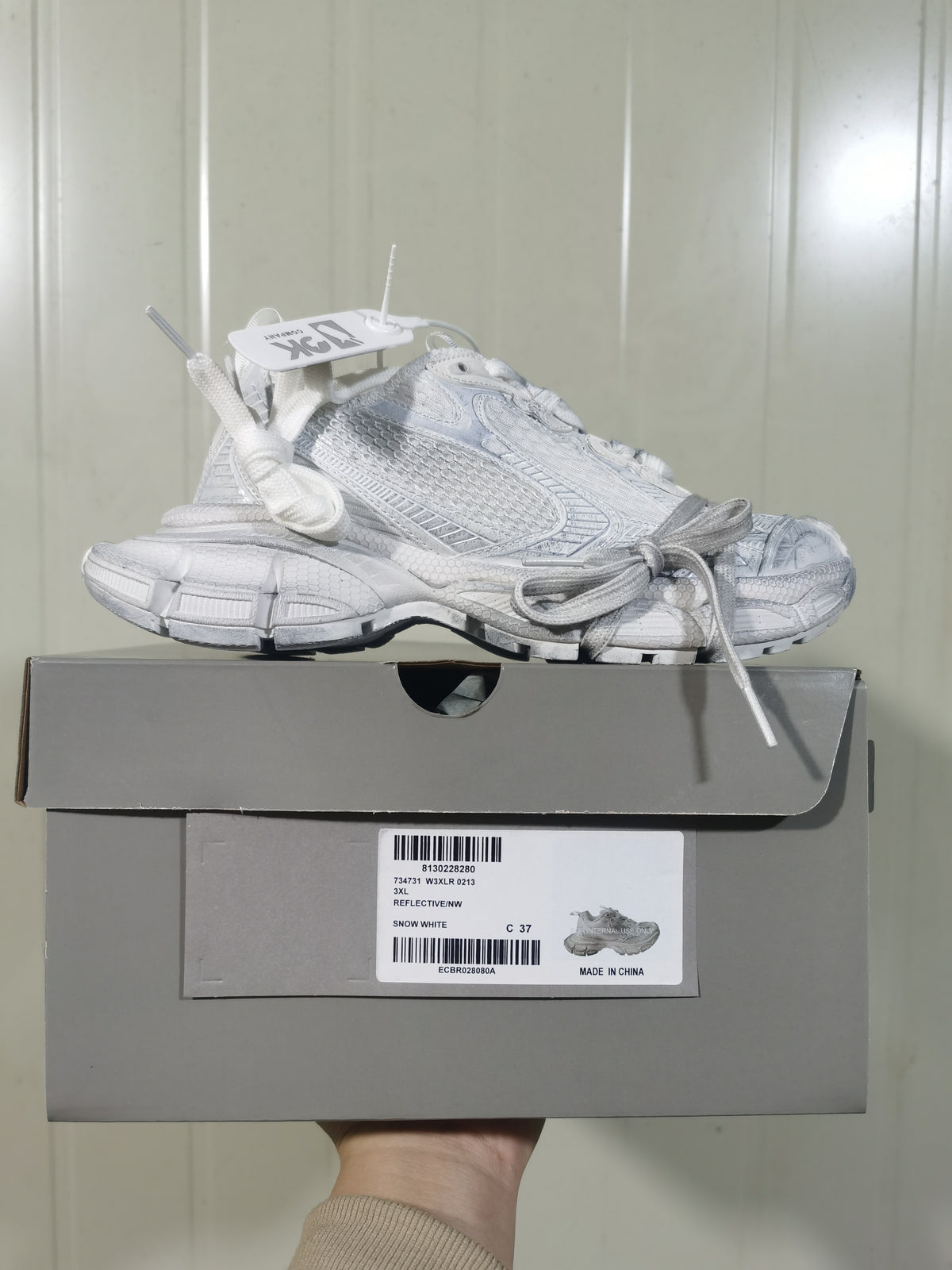 White Nike sneaker displayed on its box, showing the side profile, layered upper, chunky outsole, and box label.