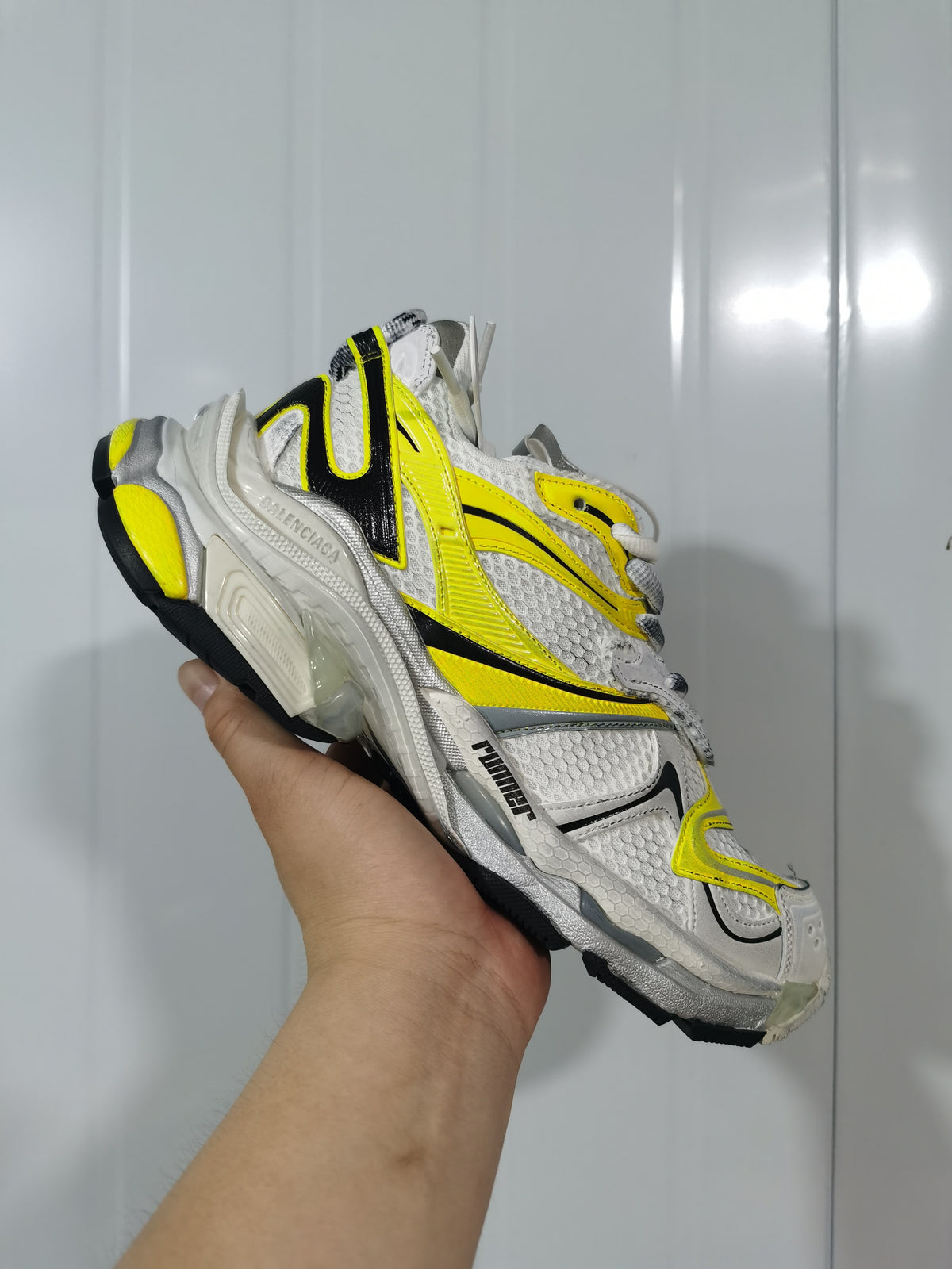 Close-up view of a white, yellow and black Balenciaga Runner 2 sneaker showing layered side panels, mesh-style detailing and a chunky outsole.