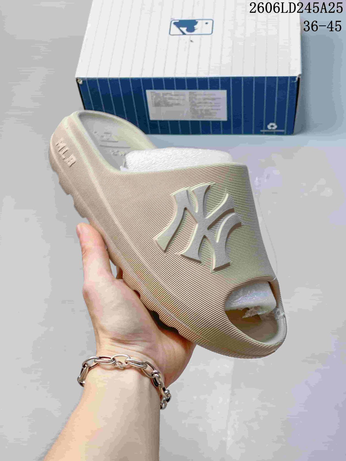 Angled close view of a beige MLB slide sandal showing the raised letter logo, open toe, and thick sole.