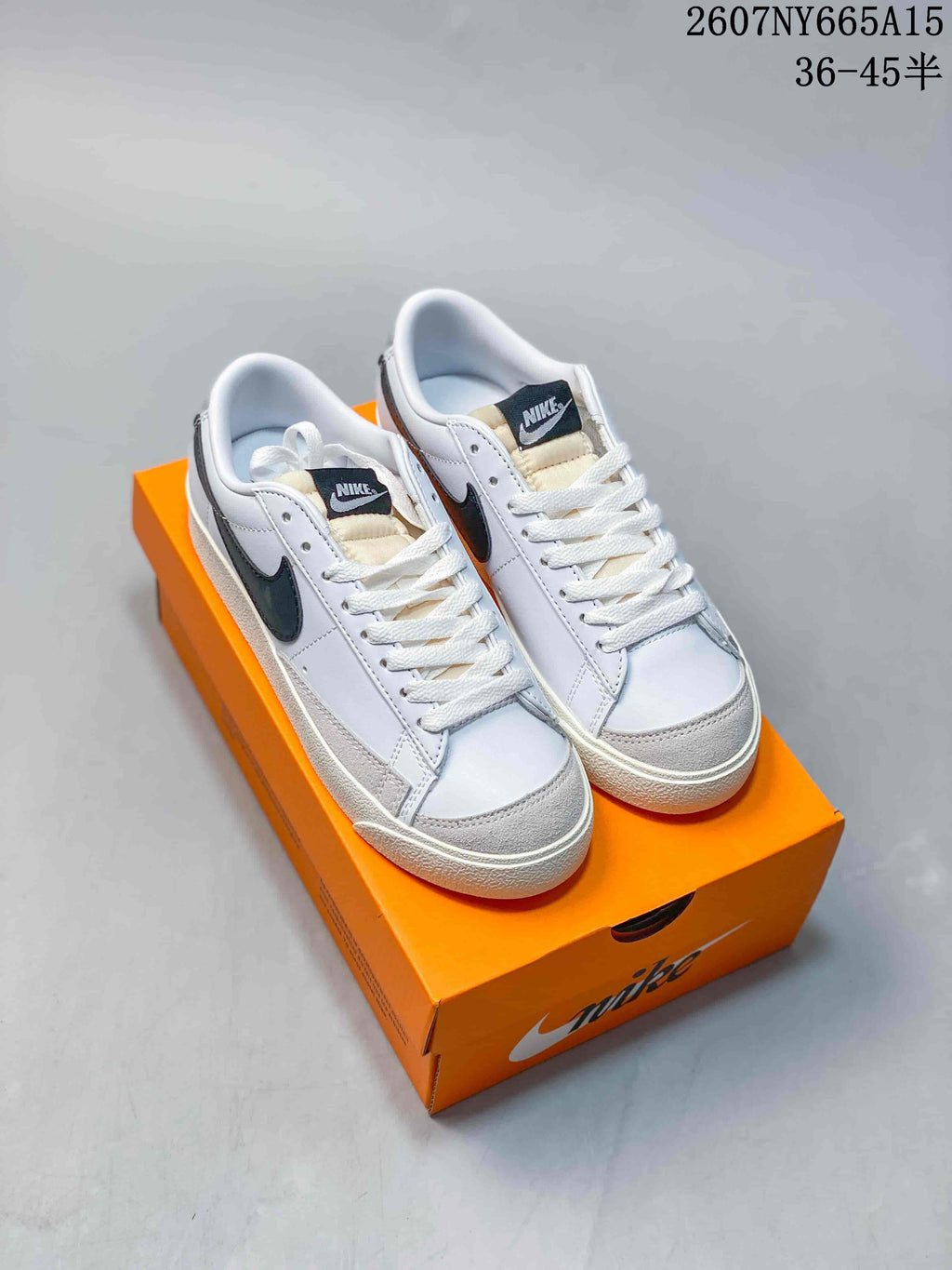 Pair of white and black Nike low-top sneakers displayed on an orange shoebox.