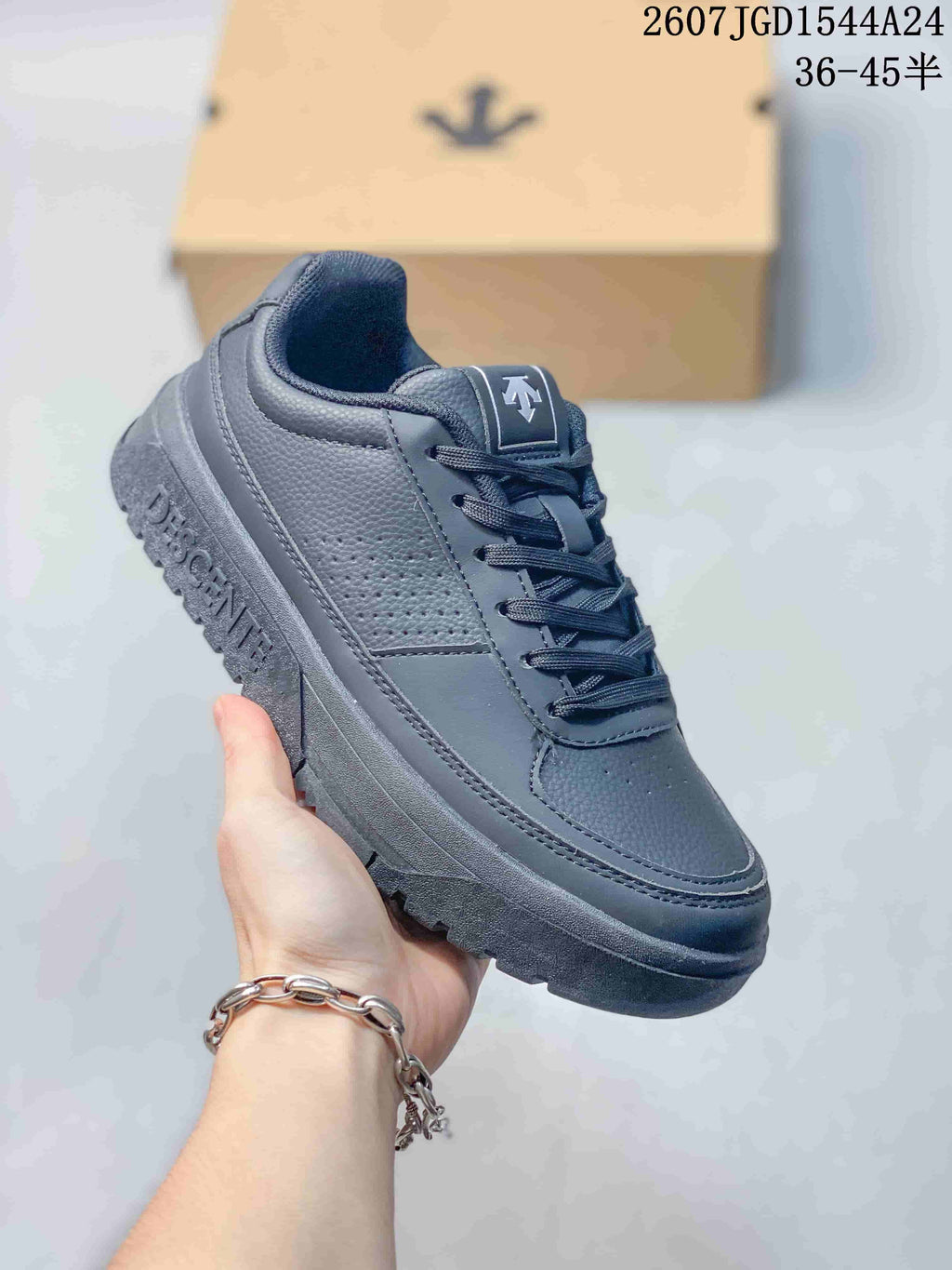 Three-quarter view of a black DESCENTE low-top sneaker showing the lace-up design, perforated side panel and textured sole.
