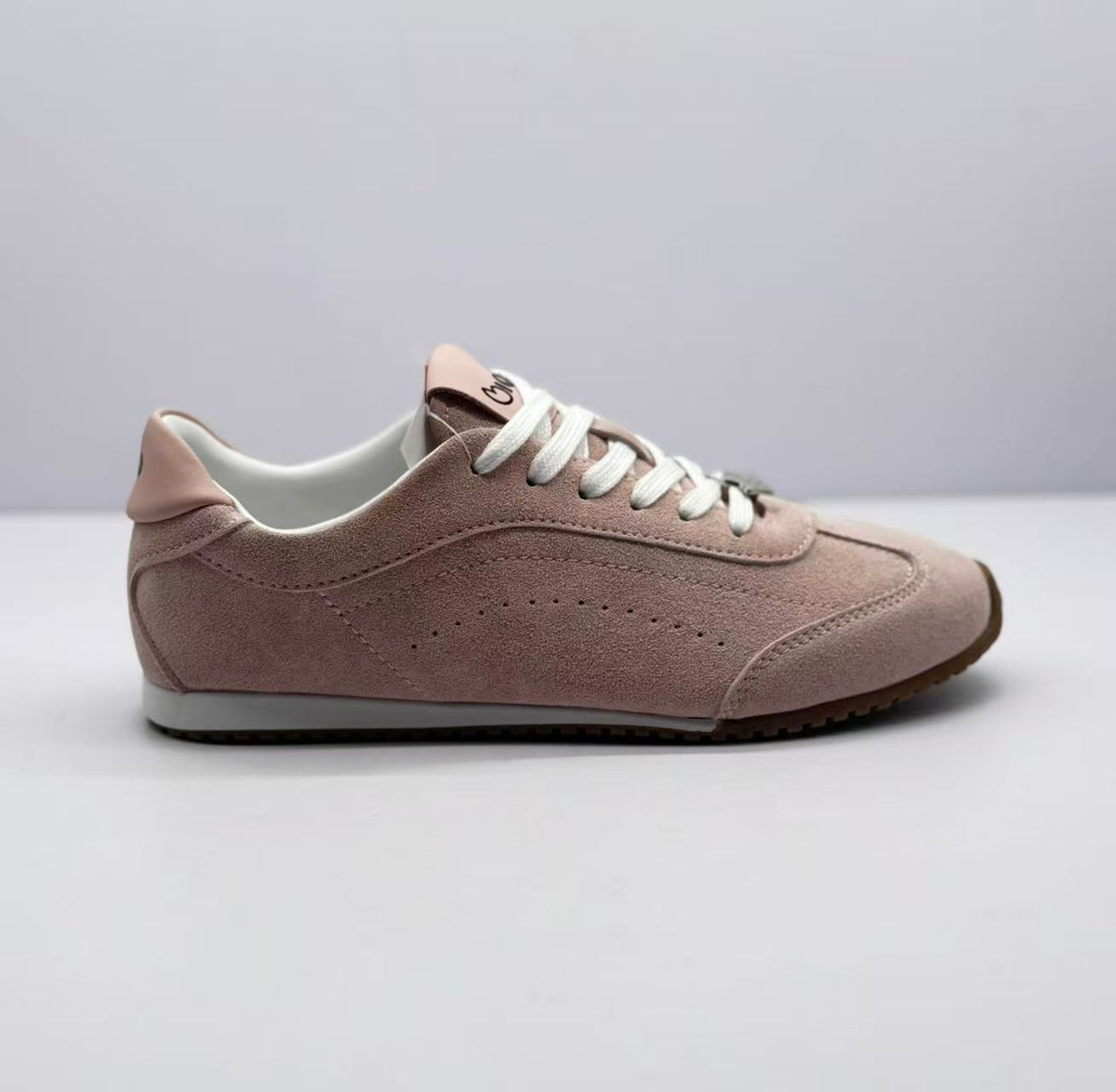 Side view of a pink low-top sneaker with white laces and a brown outsole.