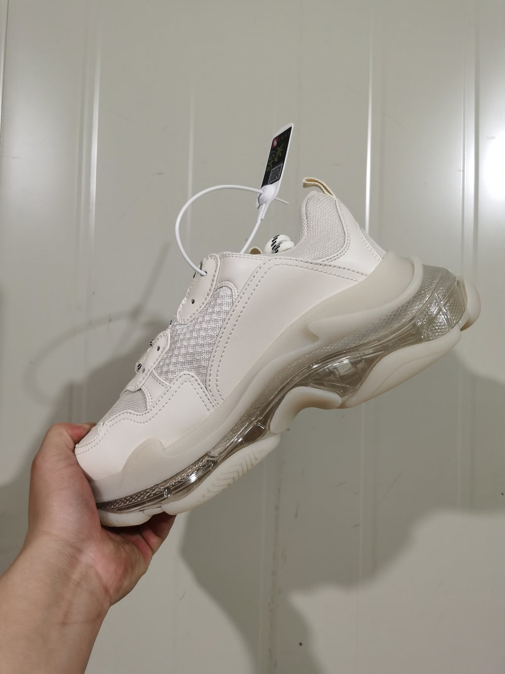 Rear three-quarter view of the white sneaker showing mesh panels, tonal overlays, and the layered clear-look sole.