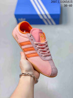 Close-up side view of a pink adidas Originals Tokyo sneaker with orange three-stripe detailing, textured gray overlays, pink laces, and a gum-colored outsole.