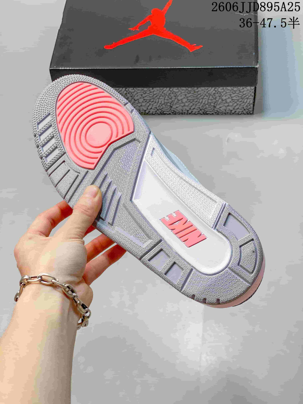 Outsole view of the sneaker showing a gray tread pattern, pink heel traction section, and a branded shoebox in the background.