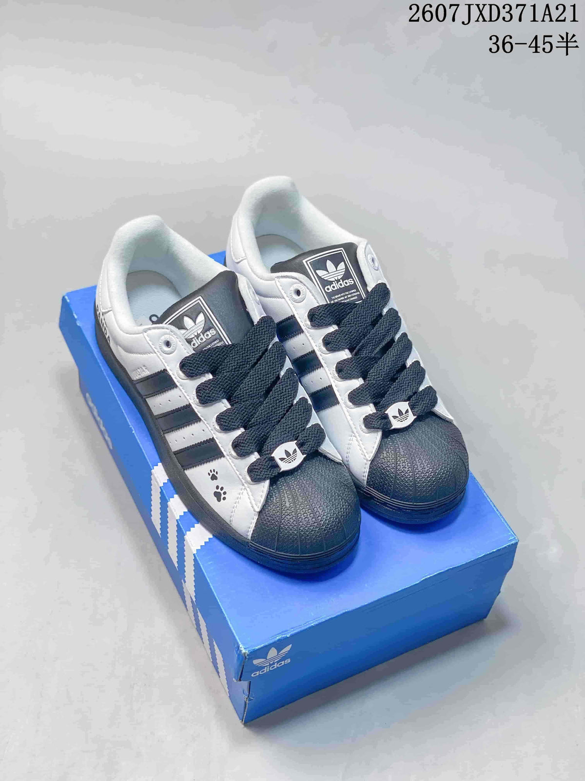 Pair of white and black adidas Superstar Supermodified sneakers displayed on a blue shoebox.
