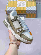White low-top sneaker with beige and olive-toned panels, shown beside a patterned box