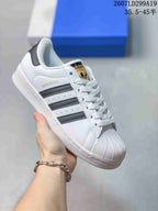 White adidas Superstar sneaker with gold branding and dark metallic serrated stripes.