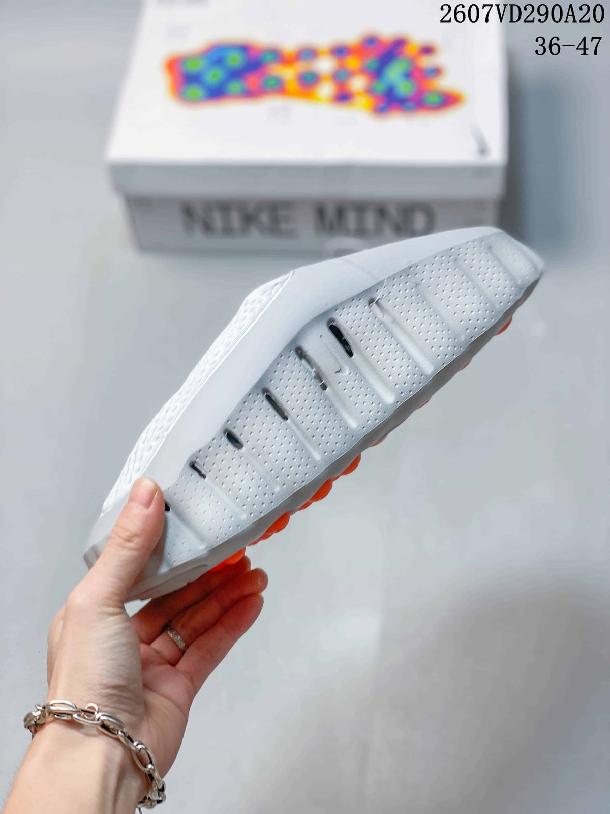 Side and outsole view of the white slide sandal, showing perforations, sculpted tread, and orange pods underneath.