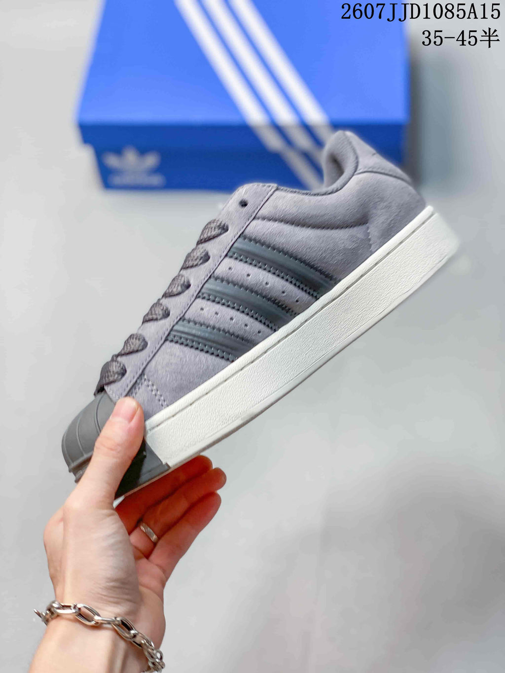 Side view of the grey sneaker showing the layered upper, three side stripes, shell toe, and raised sole.
