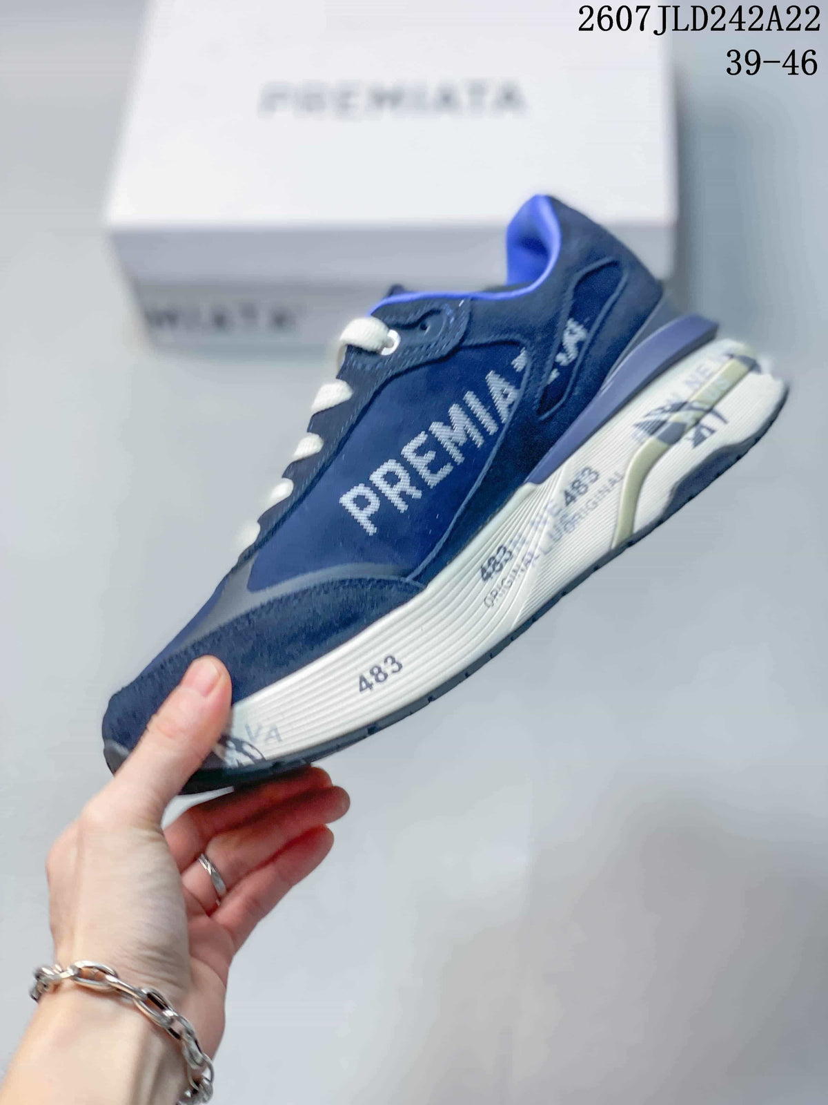 Side profile of a navy blue Premiata trainer showing layered panels, white side branding and printed midsole details.