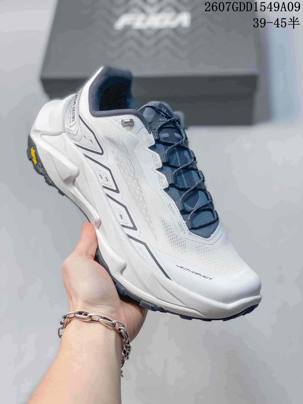 Angled side view of the white and navy shoe showing the mesh-like upper, lace system, sculpted midsole and lugged outsole.