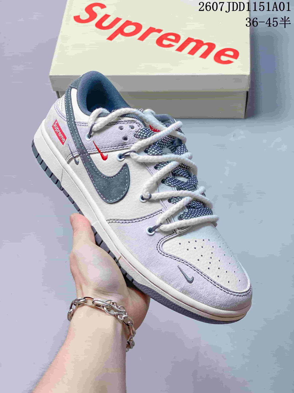 Close-up of a white and gray low-top sneaker with dark swoosh accents, patterned laces, and contrast details.