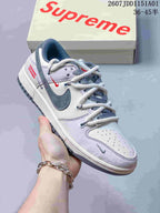 Close-up of a white and gray low-top sneaker with dark swoosh accents, patterned laces, and contrast details.