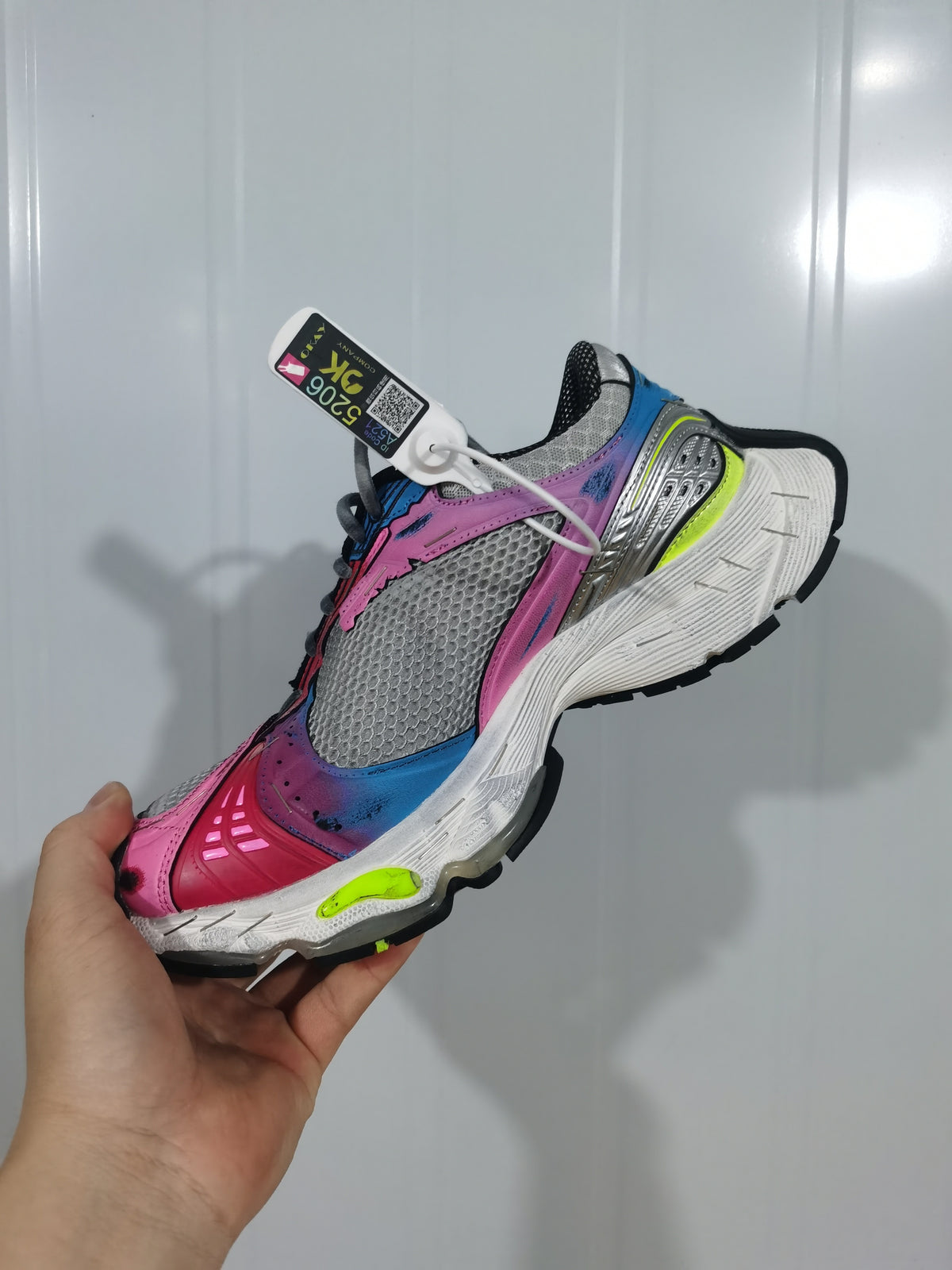 Angled view of the multicolor sneaker highlighting the mesh upper, pink toe overlay, blue details, metallic silver side panel, and black outsole.