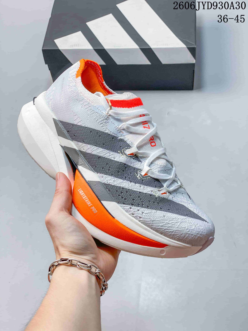 White and gray adidas Adizero Prime X3 shoe with orange sole detailing.