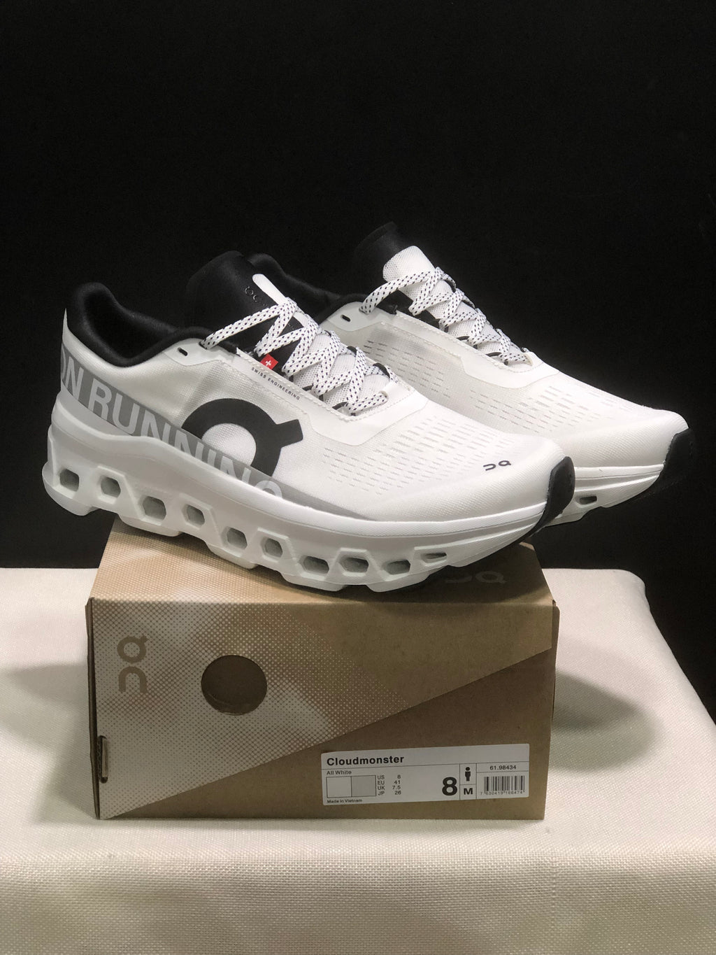 White and black On Cloudmonster sneakers displayed on a branded box, with the box label visible.