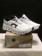 White and black On Cloudmonster sneakers displayed on a branded box, with the box label visible.