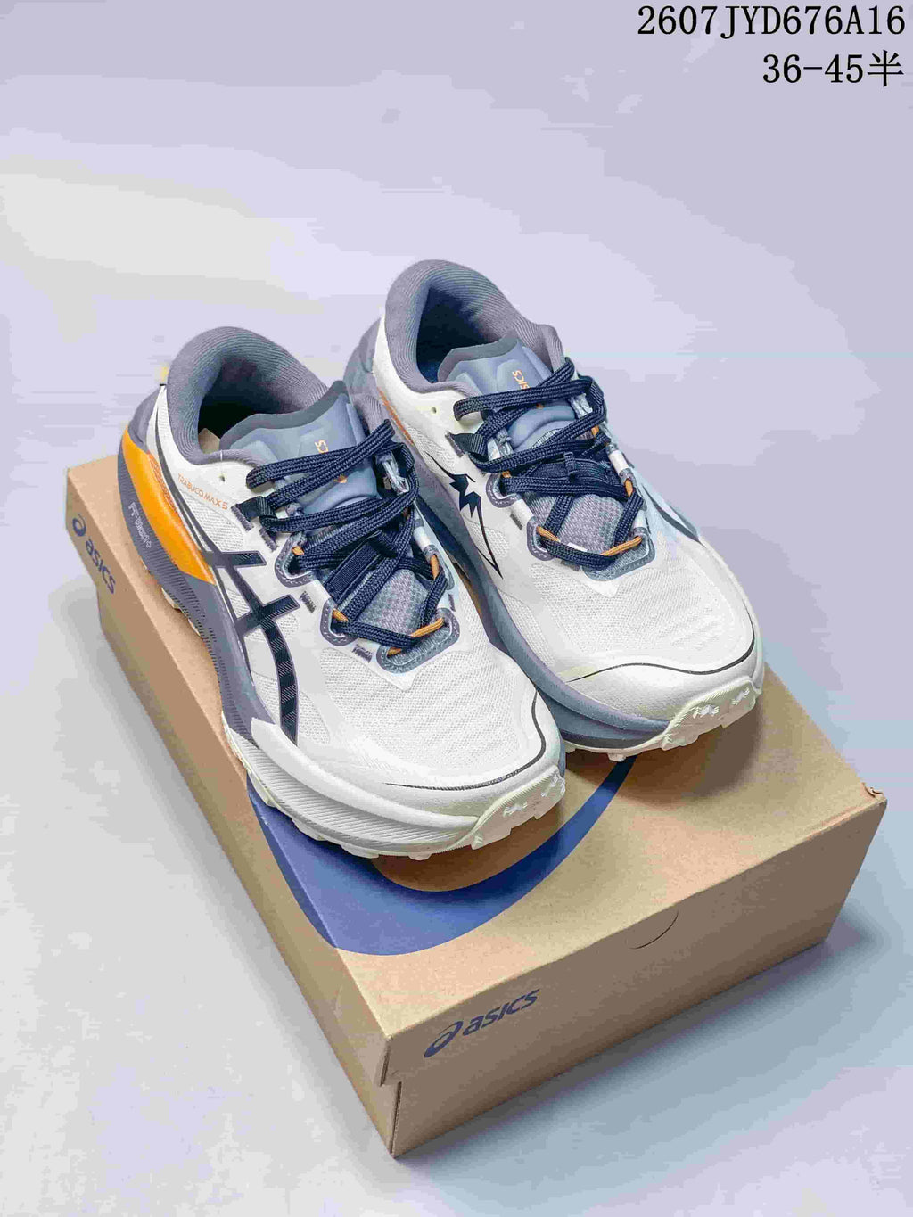Pair of ASICS Trabuco Max 5 shoes in white, gray, navy, and orange displayed on an ASICS shoebox; source image shows the size range 36–45.