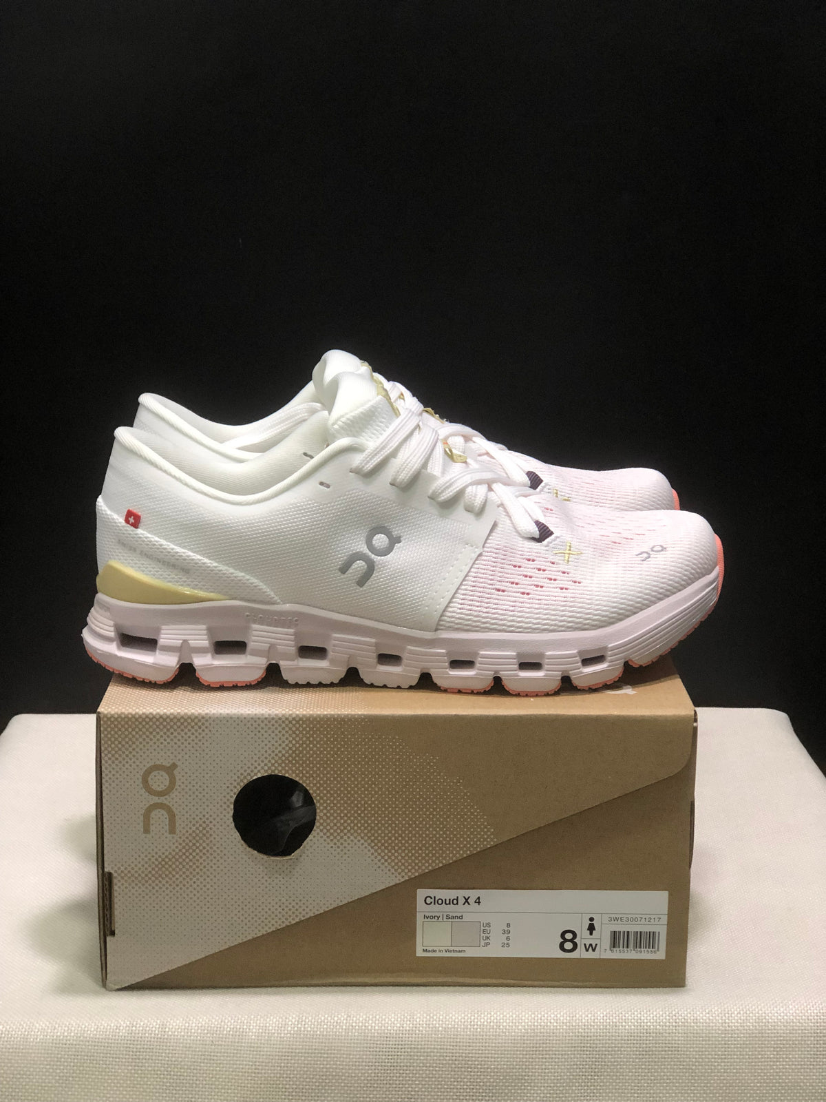 Side view of the ivory On Cloud X4 shoes showing the textured upper, yellow heel accent, and segmented sole.