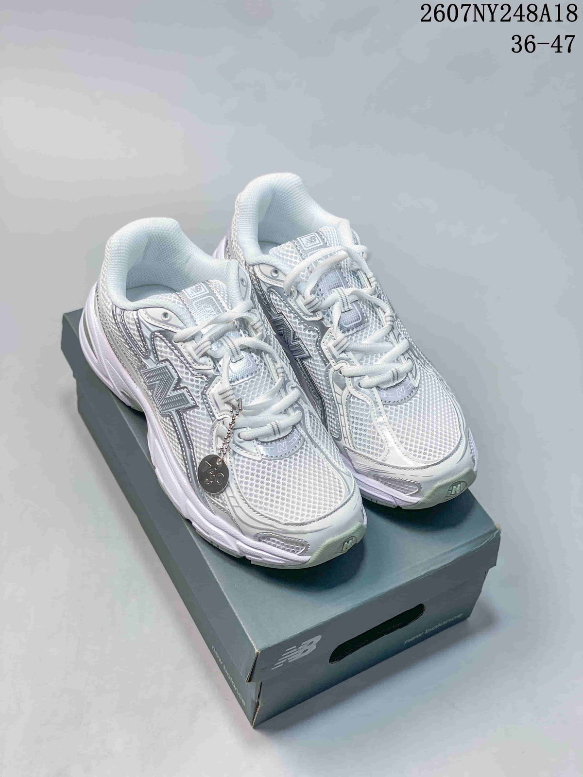 White and silver New Balance 740 sneakers displayed on a shoebox from a front three-quarter angle.