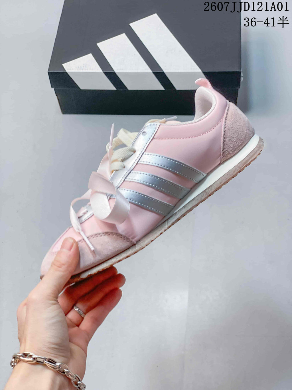 Side view of a pink sneaker with metallic silver stripes and ribbon laces