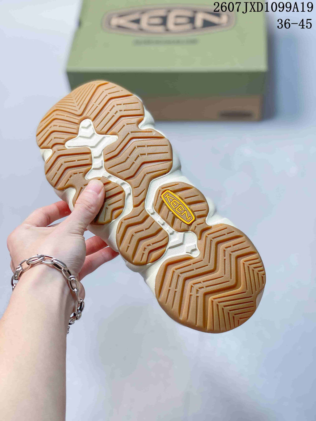 Underside view of a sandal showing the segmented cream outsole and gum-colored textured tread.