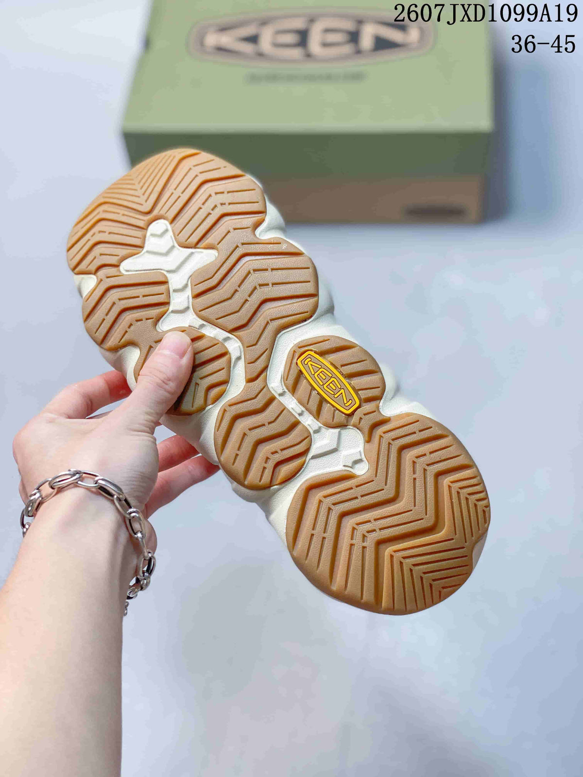 Underside view of a sandal showing the segmented cream outsole and gum-colored textured tread.